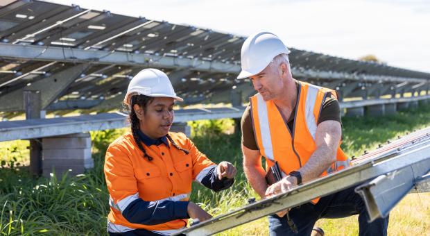 Two workers in high viz and hardhats working on solar panels.