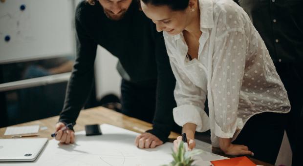 Two people looking over paper designs in a modern office environment.